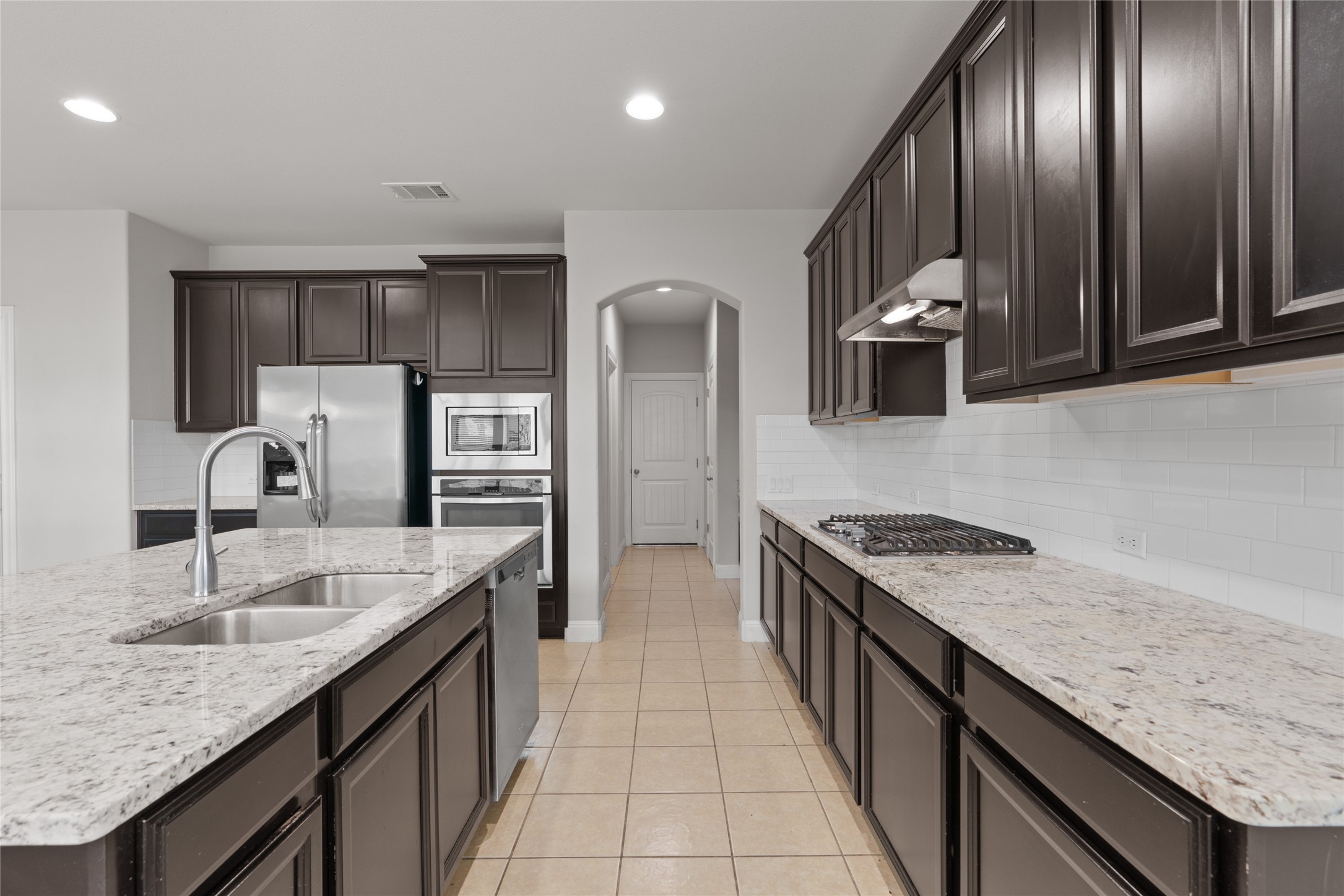 15601 Cabrillo Way Austin, TX 78738 - Photo 12 of 32 Kitchen featuring dark wood cabinetry, light granite countertops, stainless steel appliances, a double basin sink, and a gas cooktop with an overhead range hood