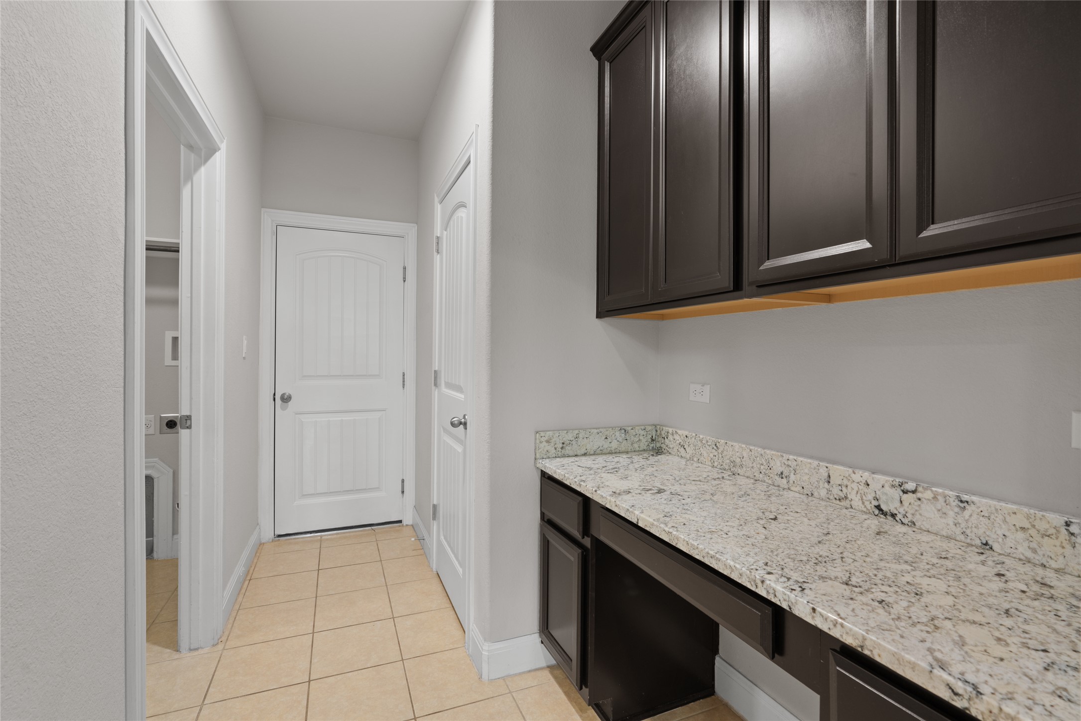 15601 Cabrillo Way Austin, TX 78738 - Photo 15 of 32 Utility area featuring extensive light-toned stone-finish countertops, dark wood-finish cabinetry, and neutral tile flooring
