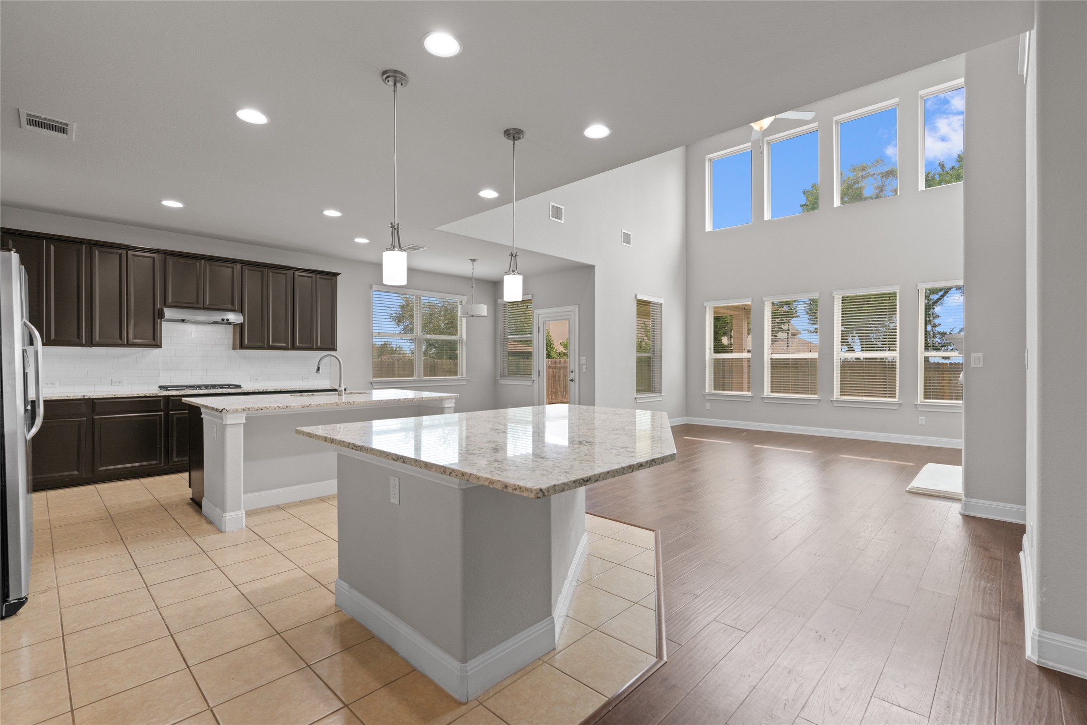 15601 Cabrillo Way Austin, TX 78738 - Photo 9 of 32 Open-concept living space featuring a two-story ceiling, extensive window arrangement, wood-finish flooring, two kitchen islands with granite countertops, and dark wood cabinetry