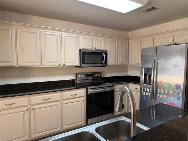 a kitchen with granite countertop a refrigerator stove and white cabinets