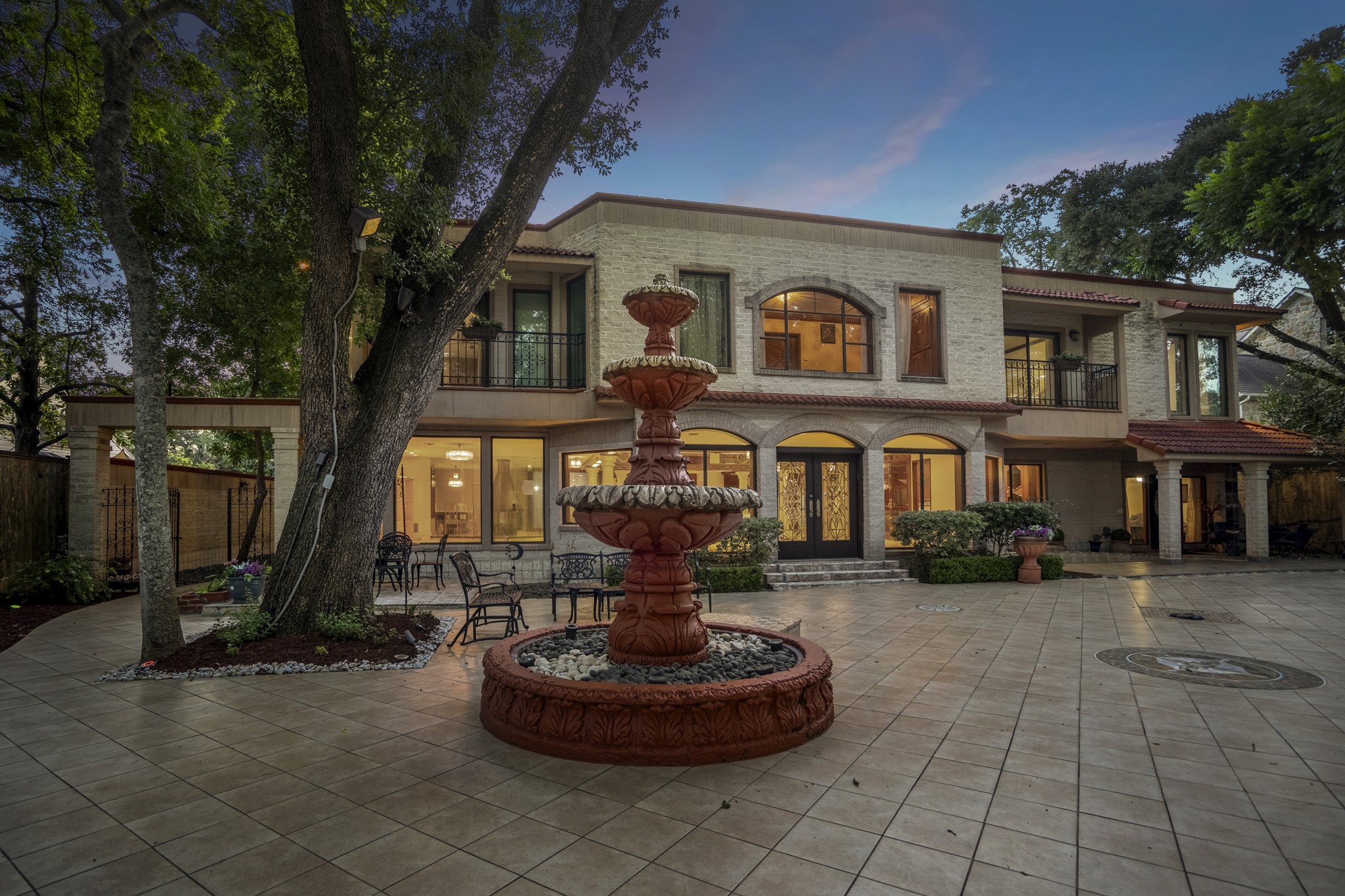 6535 Buffalo Speedway Houston, TX 77005 - Photo 32 of 34 At dusk, the fountain and courtyard glow with soft lighting, transforming the backyard into a private, resort-like Mediterranean retreat.