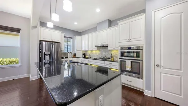 a kitchen with stainless steel appliances granite countertop a refrigerator a stove and a sink with wooden floor