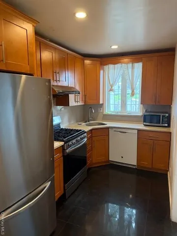 a kitchen with granite countertop a refrigerator stove and sink with wooden cabinets