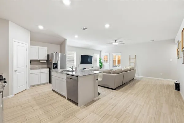 a kitchen with stainless steel appliances a stove top oven a refrigerator a sink dishwasher and white cabinets with wooden floor