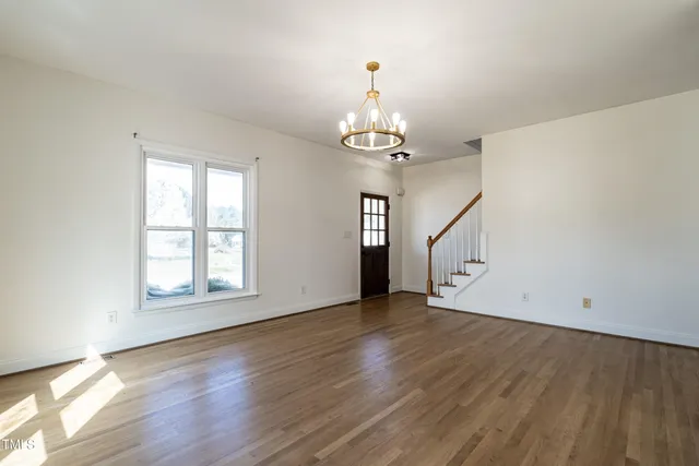 an empty room with wooden floor chandelier and windows