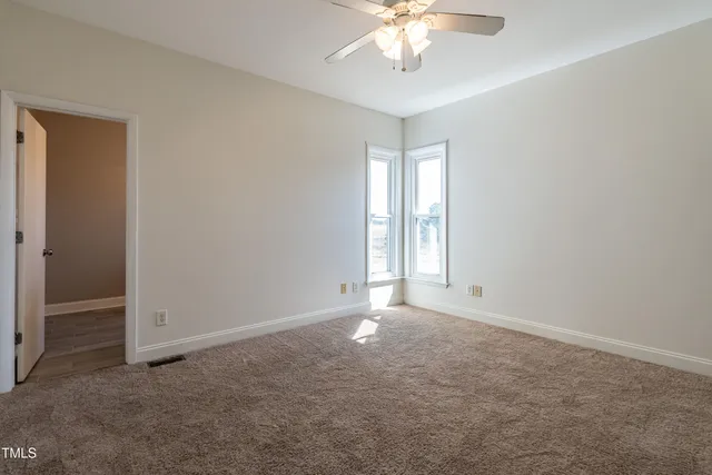 an empty room with chandelier fan and windows