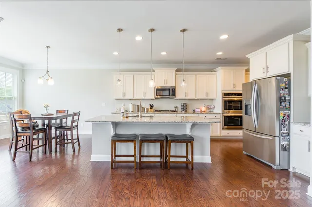 a kitchen with stainless steel appliances granite countertop a dining table chairs refrigerator microwave and cabinets