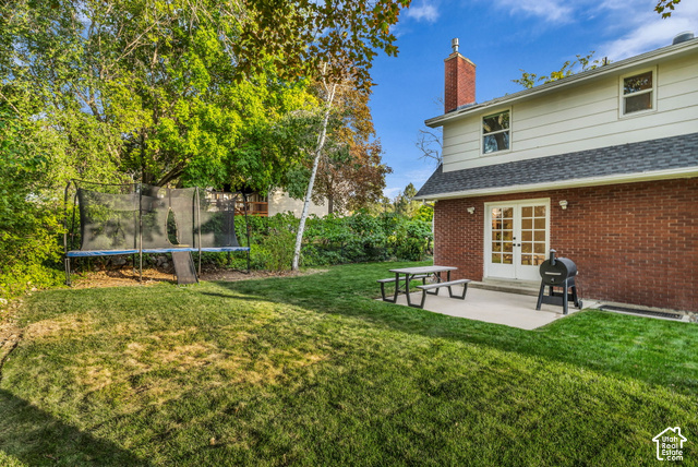 1073 Pineridge Road Sandy, UT 84094 - Photo 29 of 31 Expansive backyard featuring a manicured lawn, established perimeter trees, a concrete patio, and white French doors