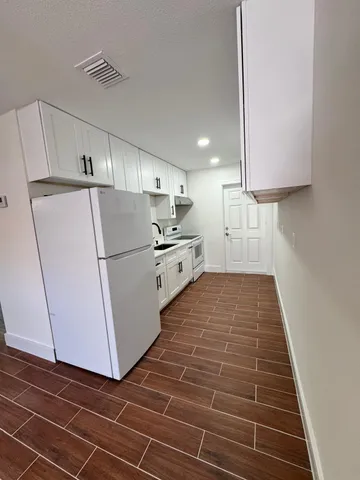 a kitchen with granite countertop a refrigerator a sink and white cabinets