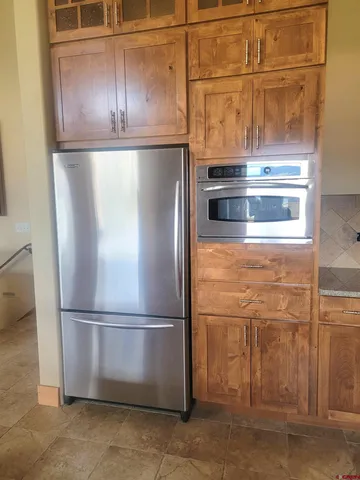 a view of a refrigerator in kitchen and an empty room with wooden floor