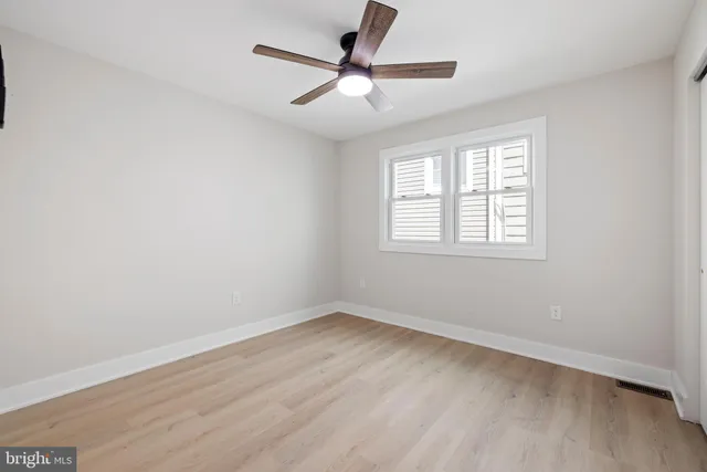 an empty room with wooden floor ceiling fan and windows