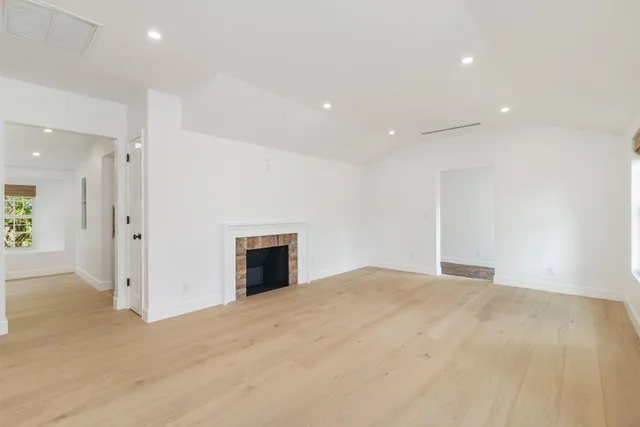 a view of an empty room with wooden floor and a kitchen