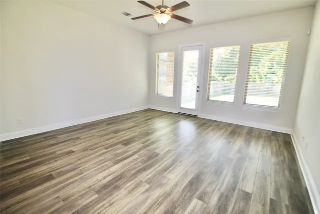 an empty room with wooden floor chandelier fan and windows