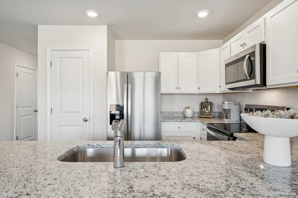 a kitchen with stainless steel appliances granite countertop a refrigerator a stove a sink and white cabinets