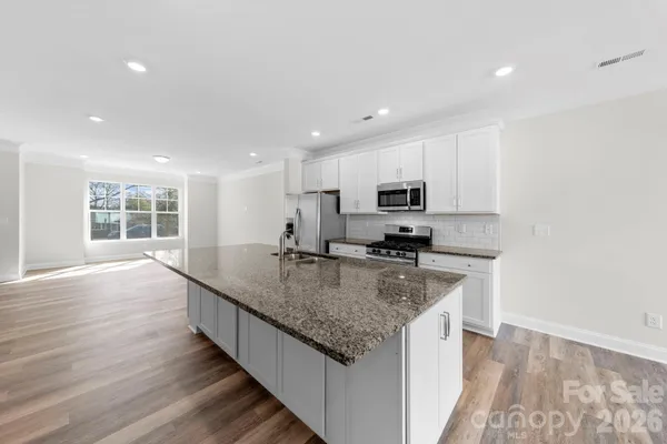 a kitchen with stainless steel appliances granite countertop a sink a stove and a wooden floors