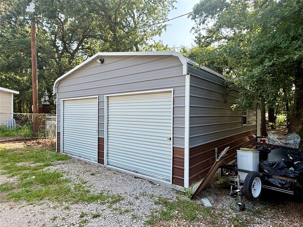 145 Adalida Lane Springtown, TX 76082 - Photo 25 of 29 Two-bay metal structure with roll-up doors, a side window, and exterior lighting, set on a gravel and grass surface