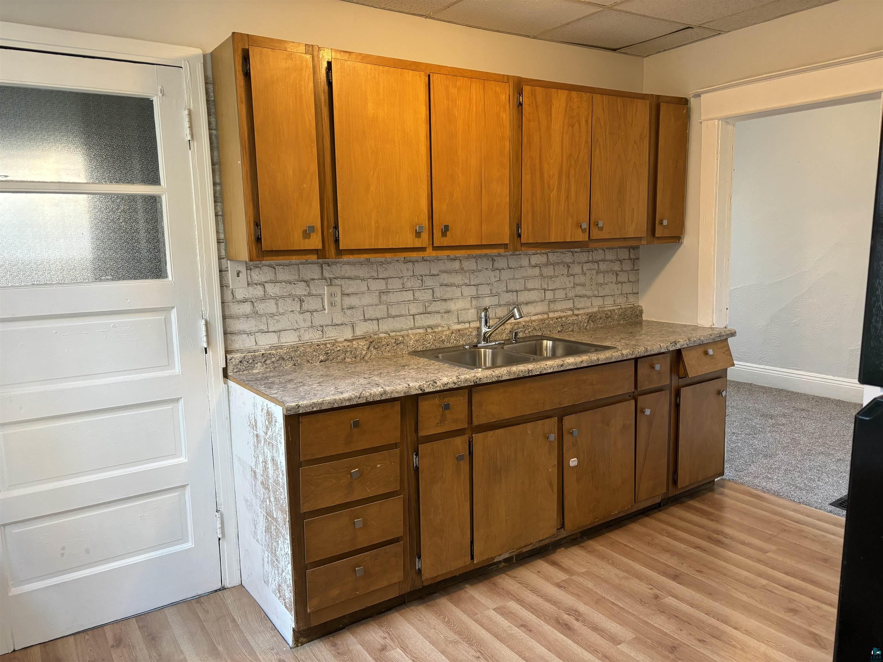 Kitchen featuring backsplash, a paneled ceiling, light wood-type flooring, and sink