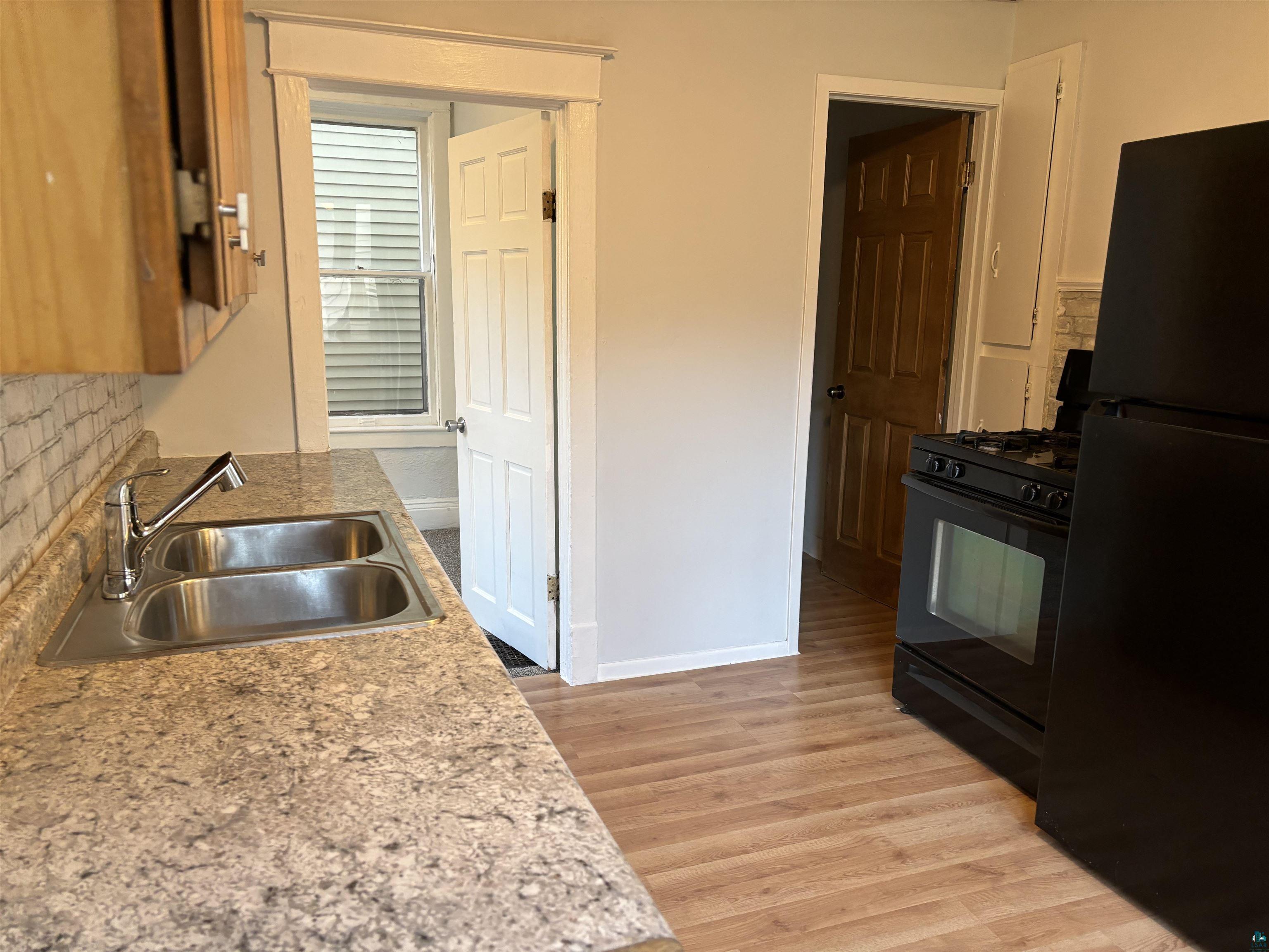 Kitchen with tasteful backsplash, sink, black appliances, and light hardwood / wood-style flooring