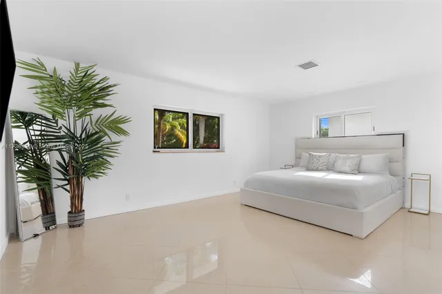 a bedroom with a large bed a flat tv screen and a potted plant