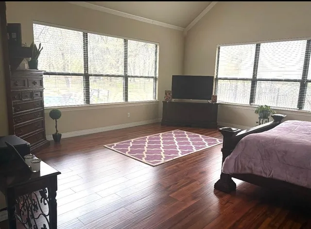 a bedroom with wooden floor and next to a window