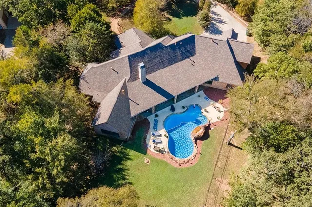 an aerial view of a house with swimming pool and large trees