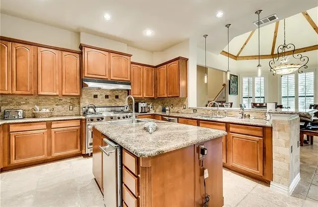 a kitchen with stainless steel appliances granite countertop a stove a sink dishwasher and a refrigerator with wooden cabinets
