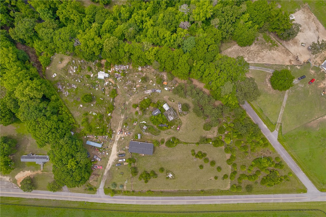 An aerial perspective showcases a spacious lot with a road, green fields, and mature trees.