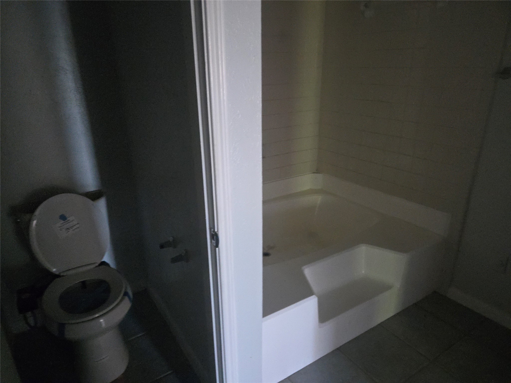 3780 Tanglewilde Street, Unit 501 Houston, TX 77063 - Photo 9 of 26 This photo shows a bathroom with a corner bathtub and a toilet. The space appears dimly lit, with tiled flooring and walls. The bathtub has a built-in seating area.