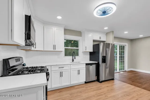 a kitchen with stainless steel appliances a refrigerator a stove a sink and white cabinets