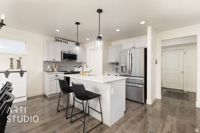 1713 South Windemere Road Santaquin, UT 84655 - Photo 10 of 40 Kitchen featuring a central island with countertop seating, light-toned cabinetry, stainless steel appliances, patterned tile backsplash, and wood-finish flooring