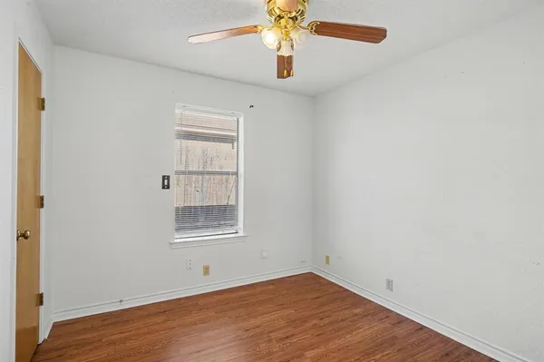 an empty room with wooden floor chandelier fan and windows