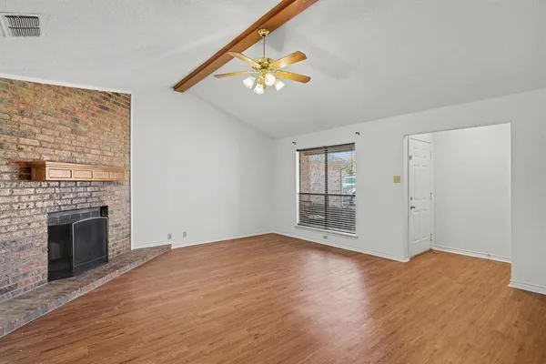a view of an empty room with wooden floor fireplace and a window