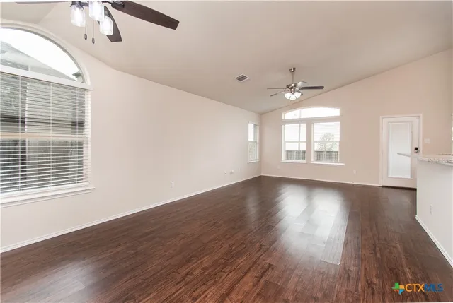 an empty room with wooden floor chandelier fan and windows
