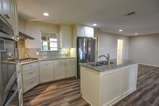 a kitchen with stainless steel appliances granite countertop a sink dishwasher a refrigerator and white cabinets with wooden floors