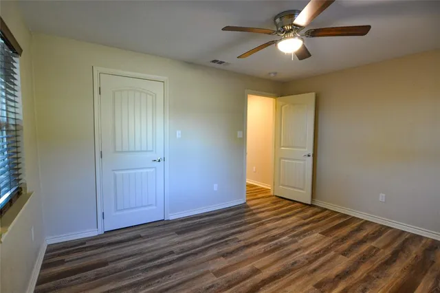 an empty room with wooden floor chandelier fan and windows