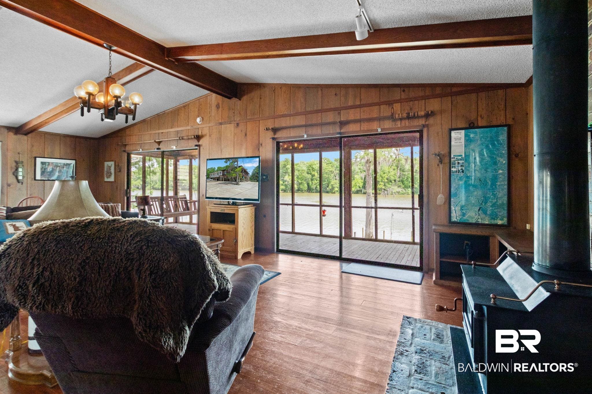 8153 Bryant's Lndg Road Stockton, AL 36579 - Photo 17 of 87 Living area featuring wood-finish walls and flooring, exposed wood beams, vaulted ceiling, and an enclosed patio with water frontage