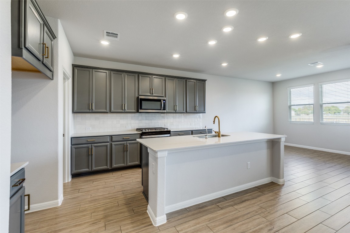 12912 Cerro Castellan Trace Manor, TX 78653 - Photo 9 of 36 a kitchen with stainless steel appliances granite countertop a sink a stove a refrigerator cabinets and a wooden floor