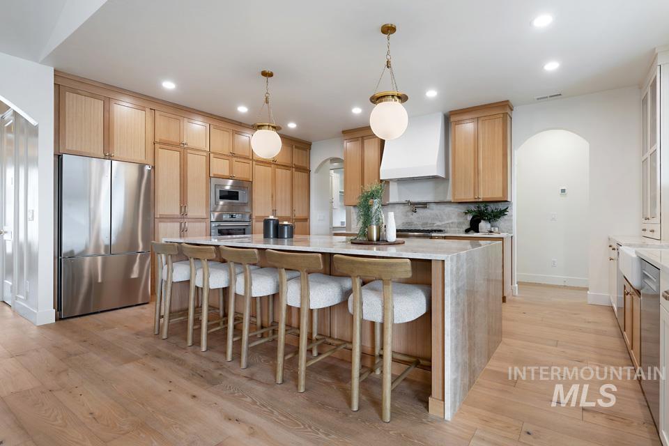 3322 South Volunteer Place Meridian, ID 83642 - Photo 13 of 50 Kitchen featuring arched walkways, appliances with stainless steel finishes, light stone counters, a kitchen bar, and custom range hood