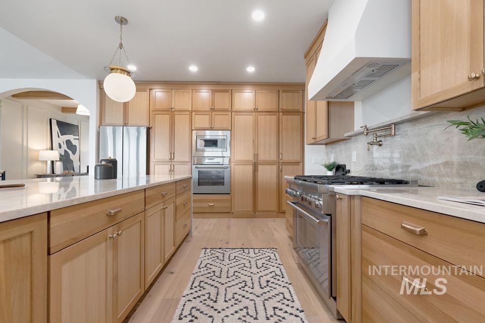 3322 South Volunteer Place Meridian, ID 83642 - Photo 20 of 50 Kitchen featuring wall chimney range hood, light stone countertops, arched walkways, appliances with stainless steel finishes, and light brown cabinetry