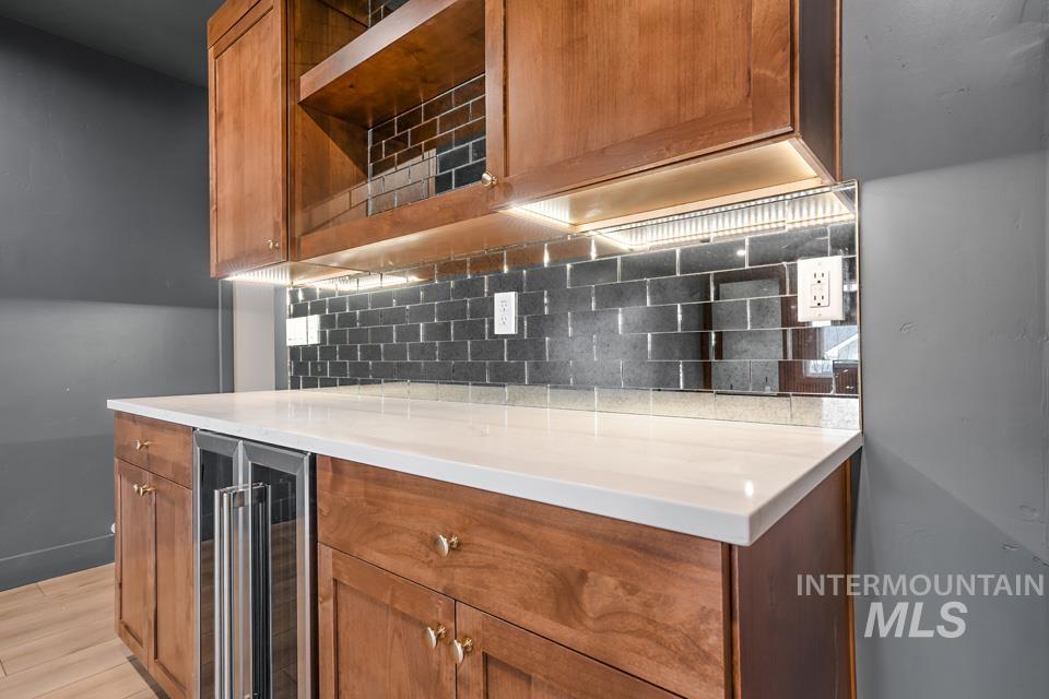 3322 South Volunteer Place Meridian, ID 83642 - Photo 45 of 50 Kitchen featuring brown cabinetry, beverage cooler, tasteful backsplash, light stone counters, and light wood-type flooring