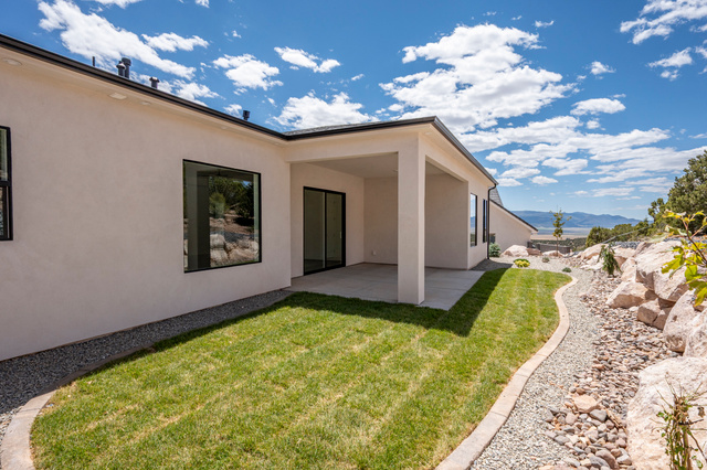 2862 South Mountain Rnch Road Cedar City, UT 84720 - Photo 53 of 64 Rear exterior featuring a covered patio, manicured lawn, and a gravel path bordered by natural rock landscaping