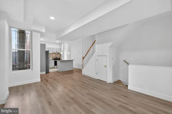 a view of empty room with wooden floor and kitchen
