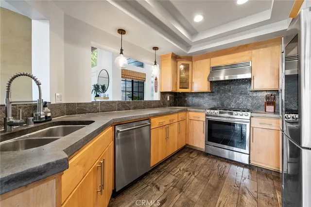 a kitchen with stainless steel appliances granite countertop wooden cabinets a stove a sink and a wooden floors
