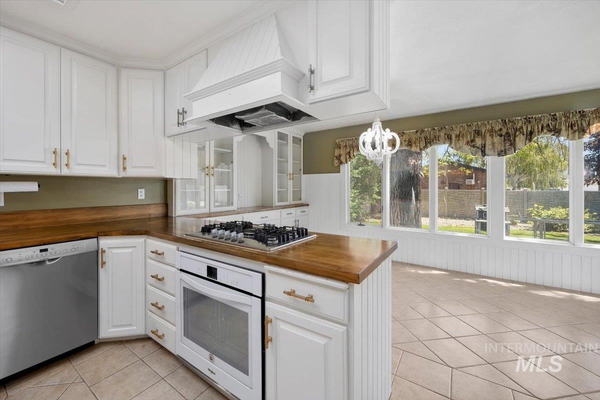 813 7th Street Rupert, ID 83350 - Photo 18 of 48 White cabinetry with gold-tone hardware, wood-finish countertops, stainless steel appliances, a built-in gas cooktop, and a wall-mounted chandelier