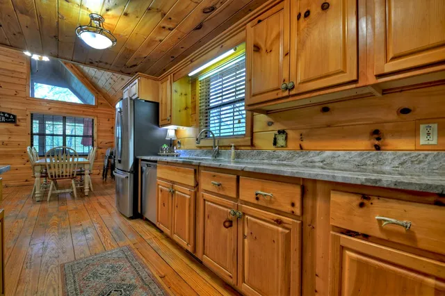 a kitchen with stainless steel appliances granite countertop a refrigerator a sink dishwasher a stove and a dining table with wooden floor