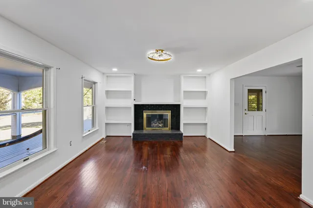 a view of an empty room with wooden floor fireplace and a window