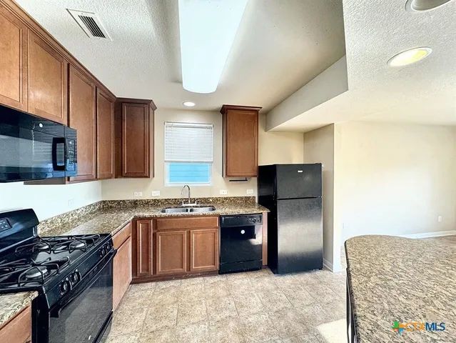 a kitchen with stainless steel appliances granite countertop a stove top oven a sink dishwasher a refrigerator and a microwave