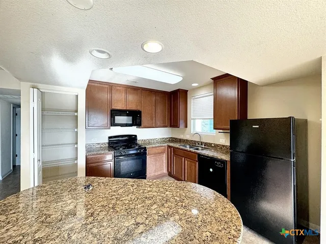 a kitchen with granite countertop a refrigerator and a stove top oven
