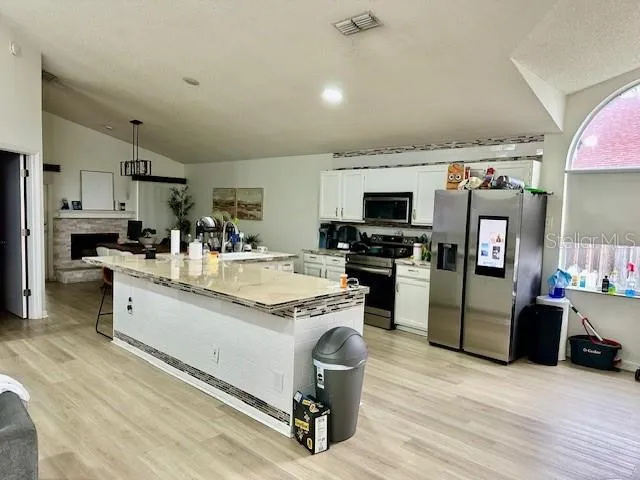 a kitchen with stainless steel appliances granite countertop a stove top oven a sink dishwasher a refrigerator and a dining table with wooden floor