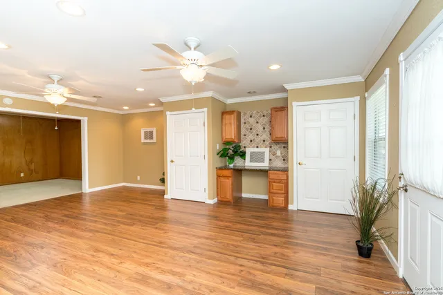 a view of an empty room and kitchen with wooden floor and fan